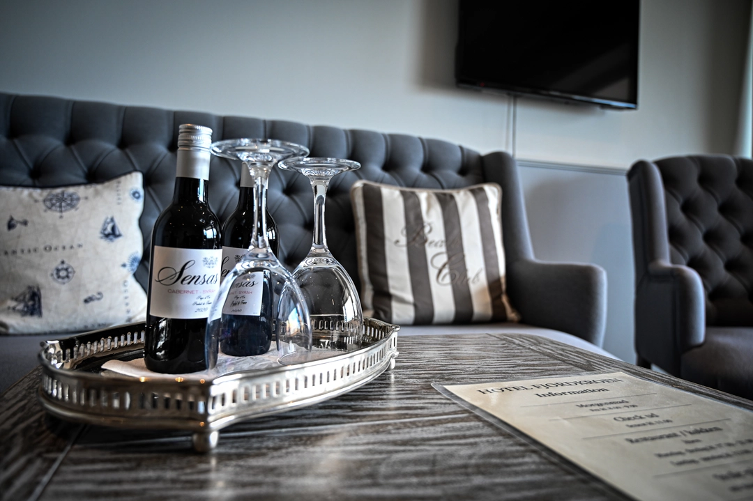 Billede af vinglas og vin fra værelsets minibar med sofa i baggrunden